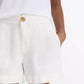 A person wearing a white short-sleeve top and vince Mid Rise Hemp Shorts in white with breathable fabric and a button closure, standing with one hand in their pocket.