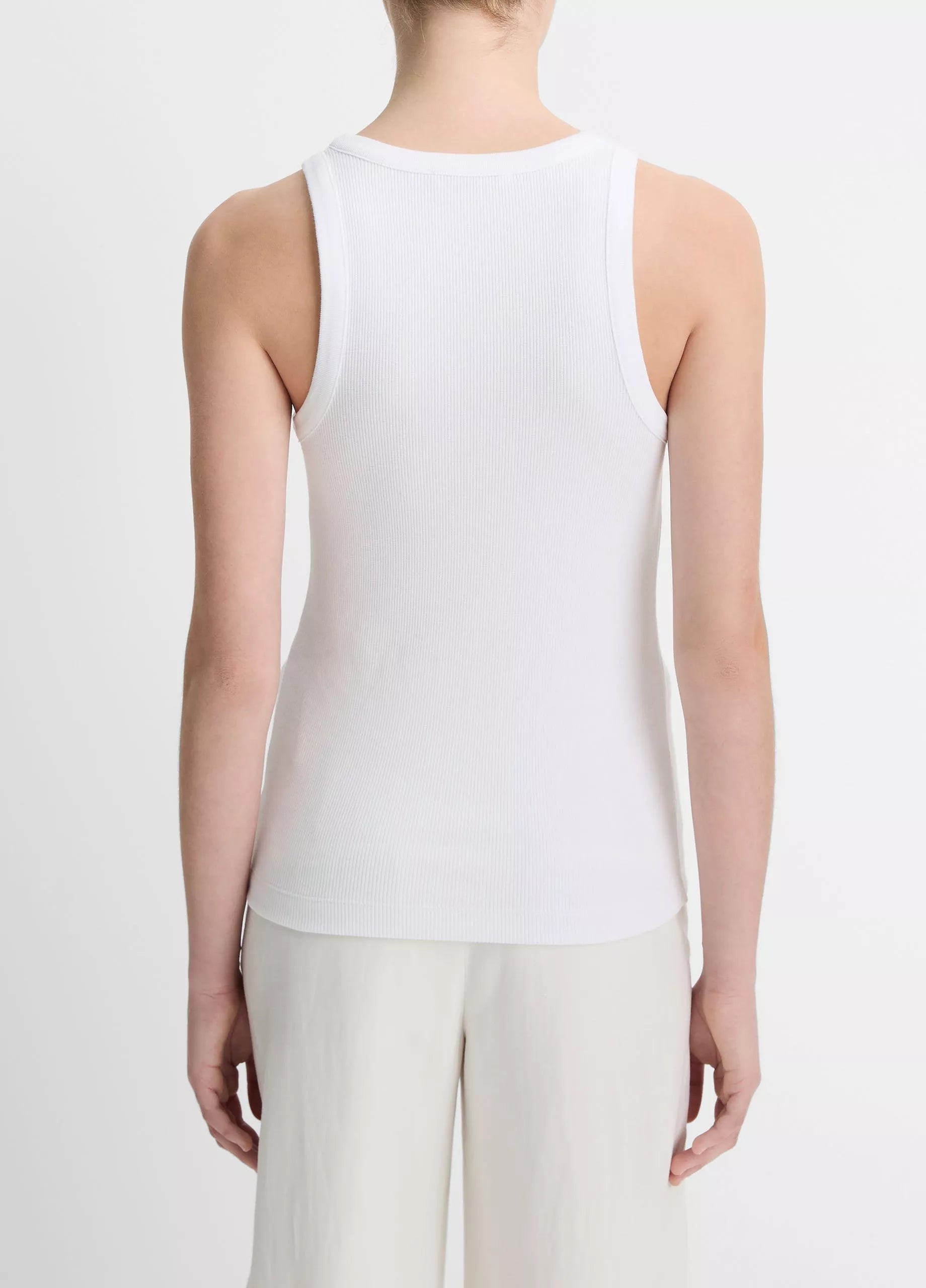 Seen from the back, the person is wearing the vince Ribbed Scoop Neck Tank—finely ribbed and sleeveless, crafted in a soft cotton modal blend—paired with light-colored pants against a plain background.