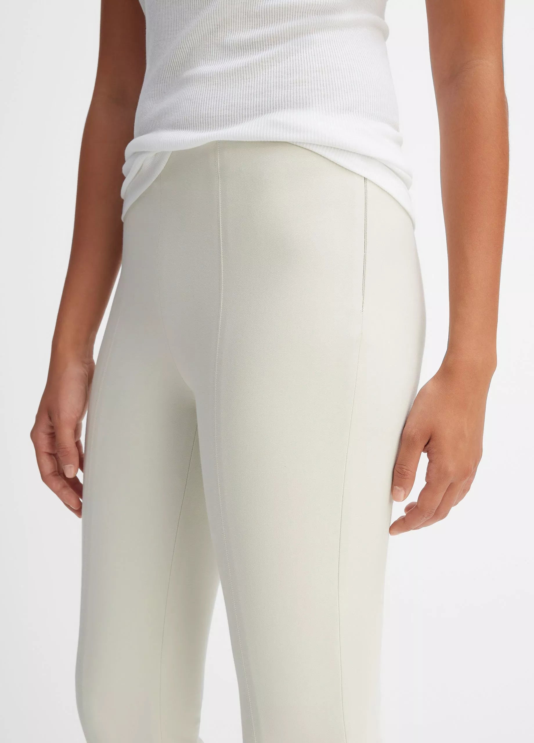 A person is shown from shoulders to mid-thigh against a plain background, wearing a white ribbed tank top and the Bobbi Mid Rise Pant by vince, crafted from a luxurious Italian cotton-blend ponte fabric.