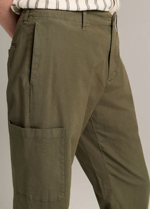 A person wearing the Owen Side Pocket Trouser by Vince in olive green, paired with a light shirt featuring dark vertical stripes, shown from the waist to knee.