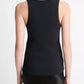 A person stands facing away in the Ribbed Scoop Neck Tank by vince— a sleeveless black tank crafted from a cotton-modal blend—paired with a black skirt, set against a plain white background.