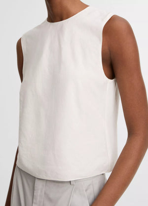 A person wears the vince Linen Crew Neck Shell Tank in white with light gray high-waisted pants, shown from shoulders to waist against a plain background. The breathable linen blend enhances comfort and offers a simple, refined look.