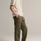 A person stands in profile wearing a short-sleeved, striped button-up shirt, the vince Owen Side Pocket Trouser in olive, and beige sneakers against a plain background.