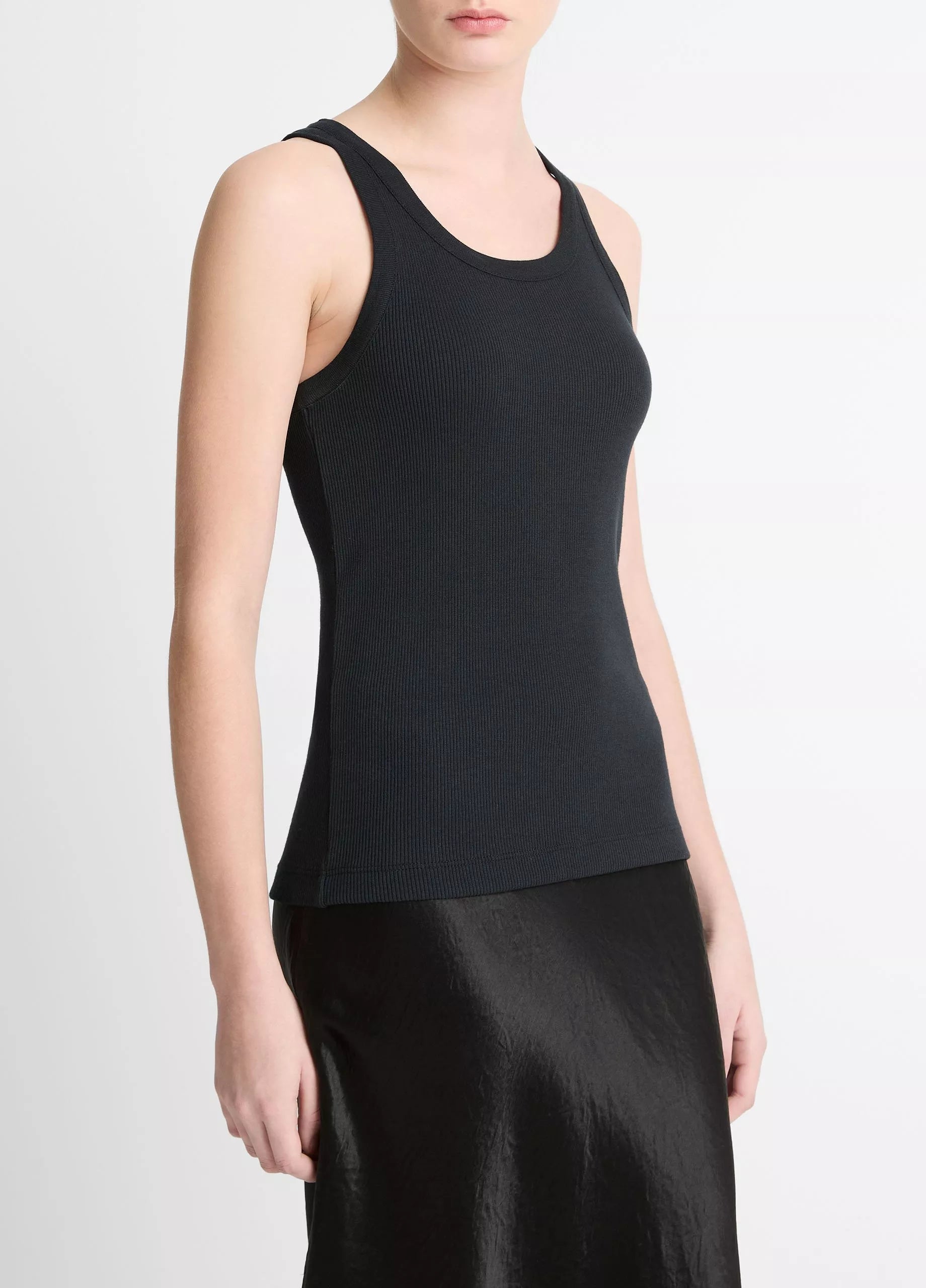 A person wearing the Vince Ribbed Scoop Neck Tank in black and a black satin skirt, shown from the shoulders to the knees against a plain background.