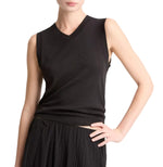 Wearing the Vince High V-Neck Shell Tank in black and a pleated black skirt, a person poses with one hand on their hip against a white background.