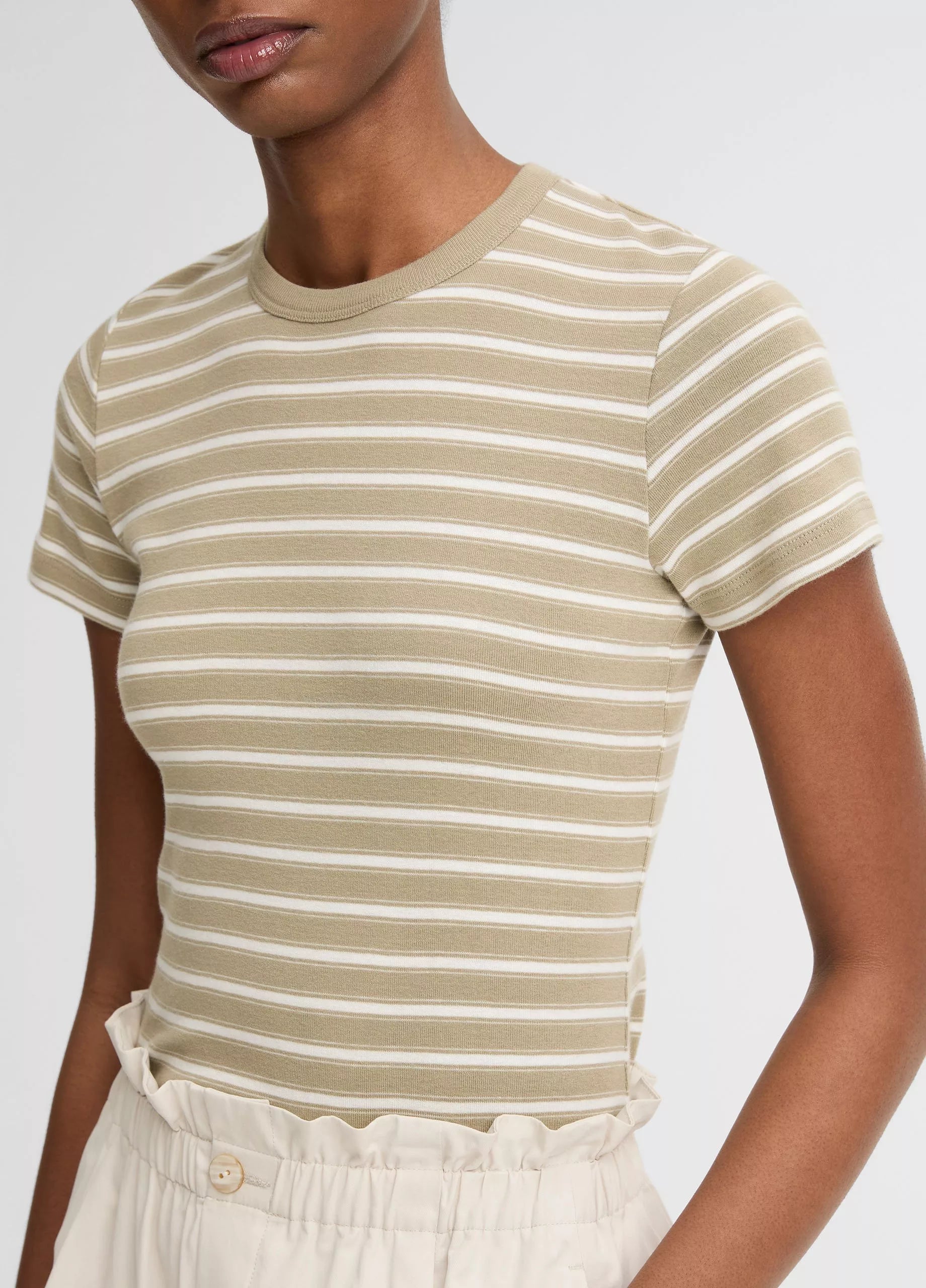 A model wears the vince Stripe Shrunken 90s Tee—a beige and white striped, shrunken-fit top—tucked into high-waisted, light-colored pants, shown from shoulders to waist.