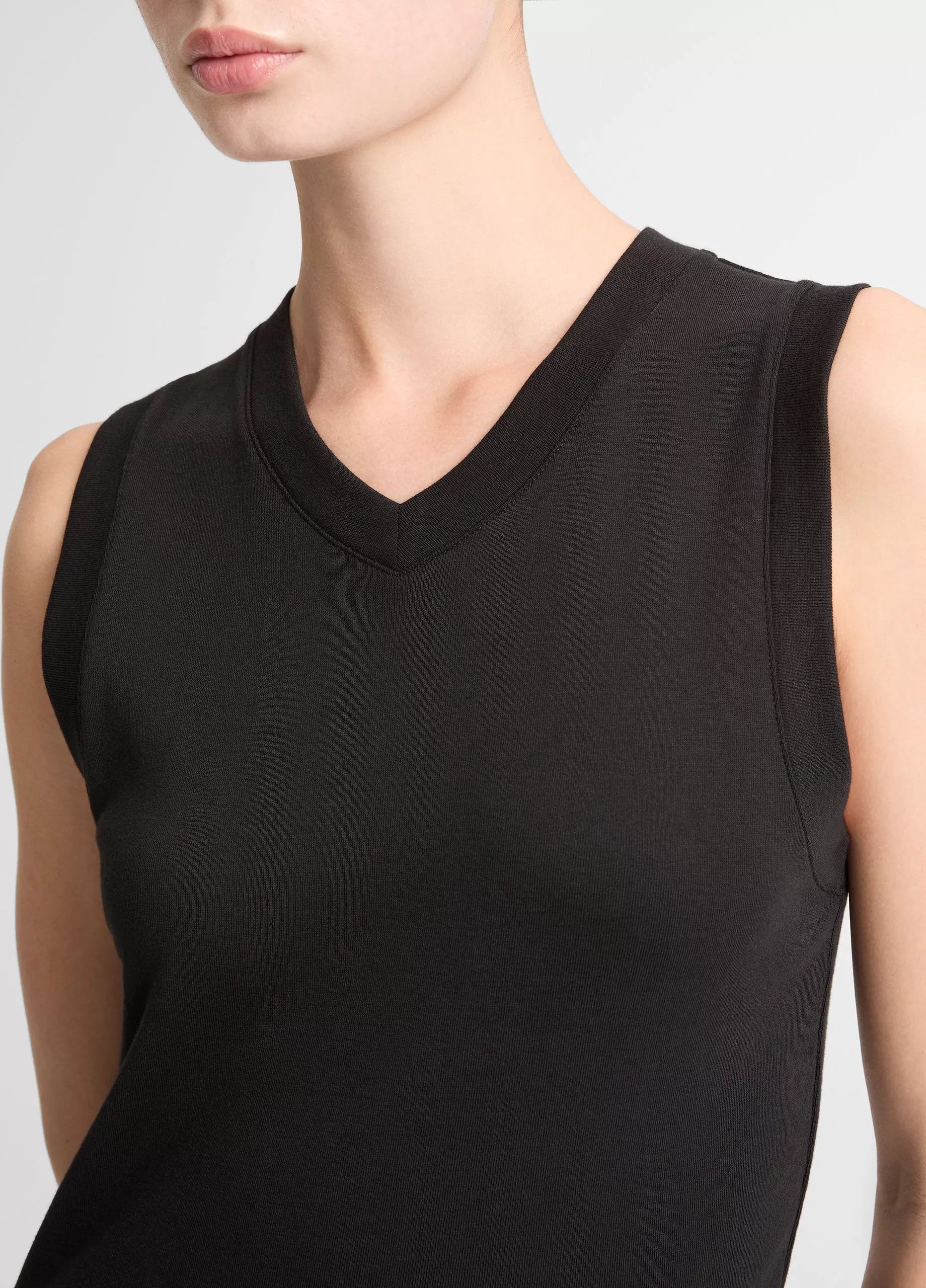 A model showcases the vince High V-Neck Shell Tank, a sleeveless black top crafted from soft Pima cotton, photographed from shoulders to mid-torso against a plain background.