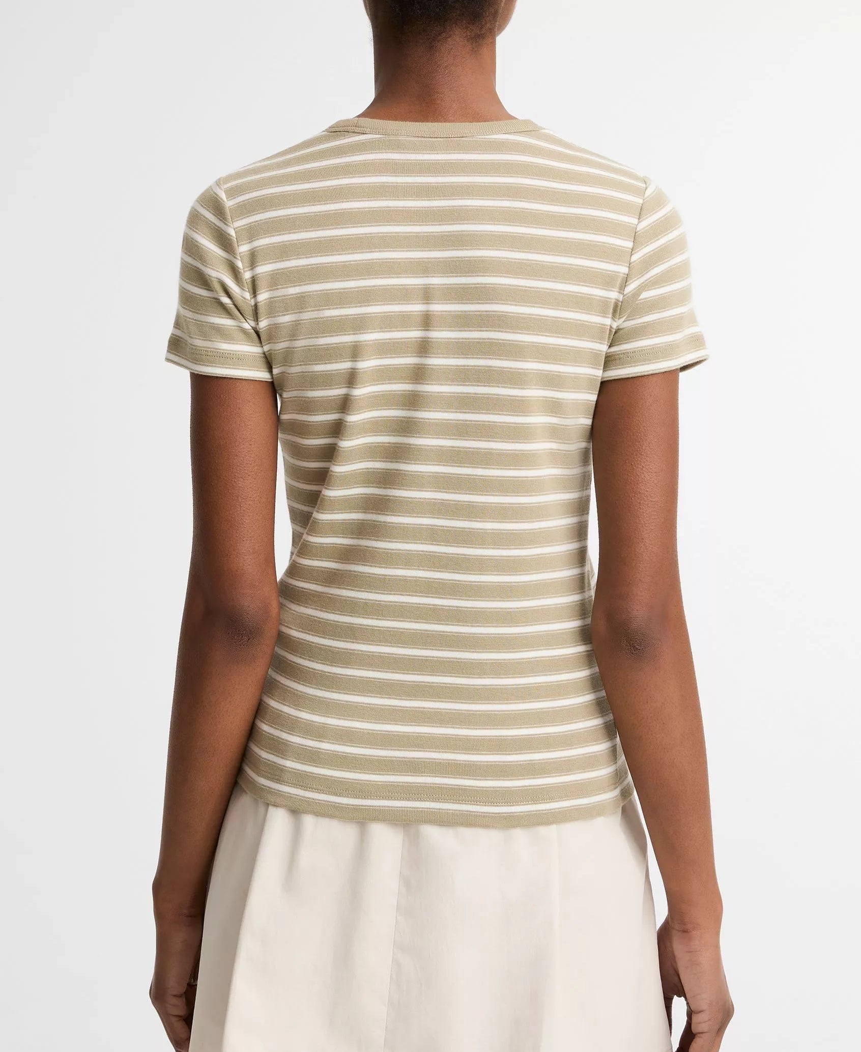 A person stands facing away, wearing the Vince Stripe Shrunken 90s Tee in beige and white stripes paired with a light-colored skirt, set against a plain background.