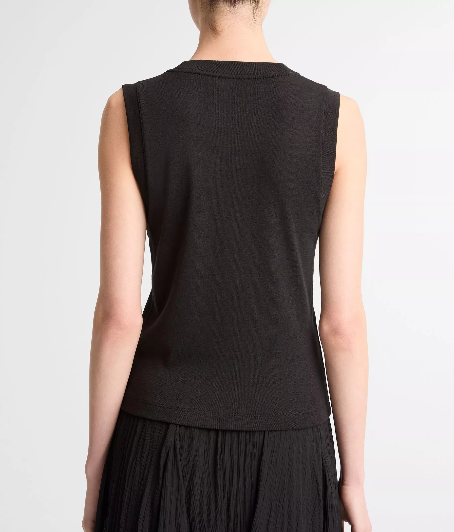 A person shown from the back against a plain light background wears the vince High V-Neck Shell Tank in black, paired with a black pleated skirt.