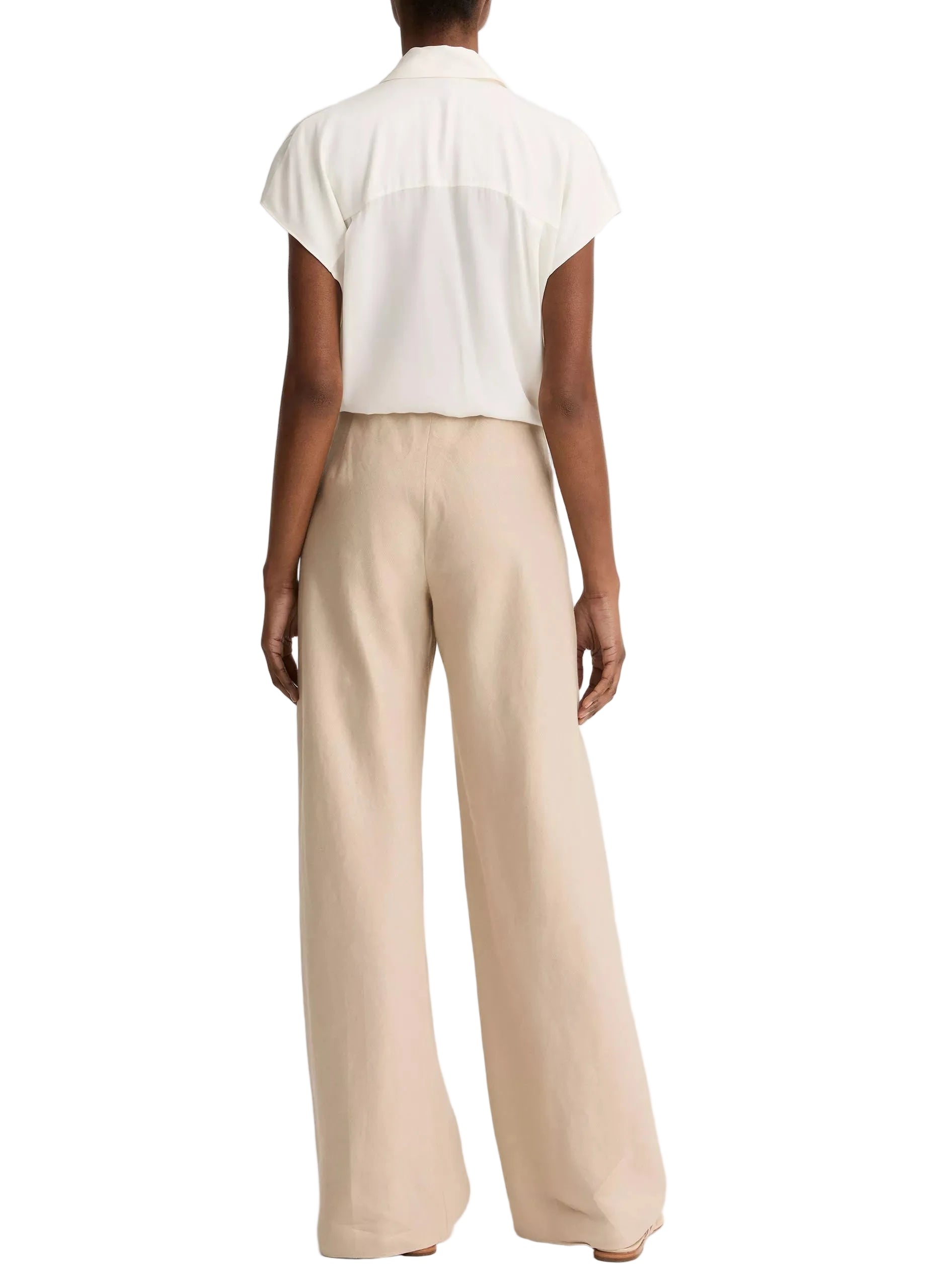 A person stands facing away, wearing a short-sleeve white blouse and the Colette Linen Bias Pant by vince—wide-leg, beige trousers made from luxurious Italian linen with a hidden elastic waistband—set against a white background.