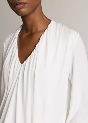 A model is shown from the shoulders to the chest against a neutral background, wearing the Vince Matte Jersey V-Neck Bubble Top in white, offering a minimal interpretation of classic style.