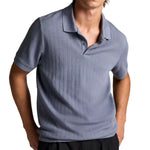 A person wearing the Vince Drop Needle Stripe SS Polo in light blue with short sleeves and black pants, standing with hands in pockets against a white background.