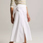 A person wearing a striped long-sleeve top, the Scarf Tie Skirt by vince—a white cotton twill midi skirt with a slit—and beige heeled sandals, standing against a neutral background.