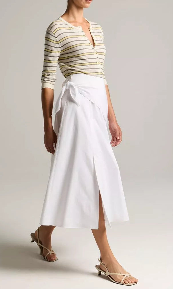 A person wearing a striped long-sleeve top, the Scarf Tie Skirt by vince—a white cotton twill midi skirt with a slit—and beige heeled sandals, standing against a neutral background.