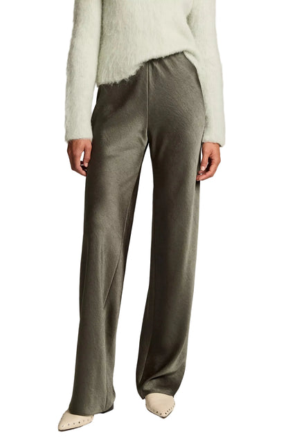 A person wearing a fuzzy light-colored sweater, the Vince Colette High Waisted Fluid Satin Bias Pant in olive green, and pointed beige shoes stands against a white background.