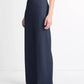 A person wearing a sleeveless black top, dark blue Colette High Waist Pant by vince with an elastic waistband, and black sandals stands against a plain white background.