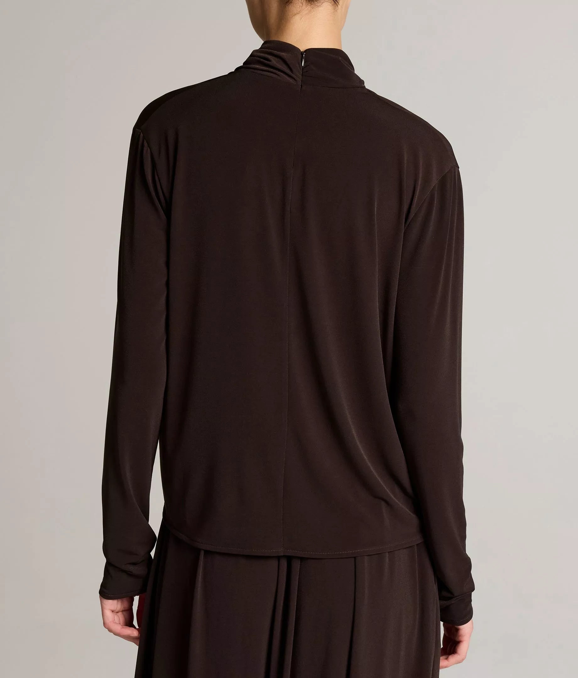 A person is seen from the back wearing the vince Long Sleeve Draped Cowl Blouse in dark brown matte jersey, featuring a center back seam and a high neckline.