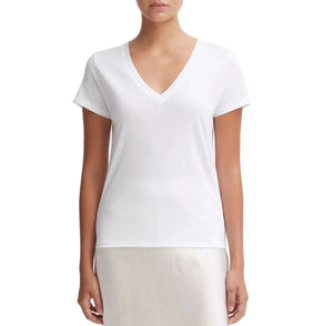 A person wearing the Vince Essential V-Neck—a white Peruvian Pima cotton T-shirt with a relaxed shape for effortless style and comfort—paired with a light-colored midi skirt and slip-on shoes, stands against a plain white background.