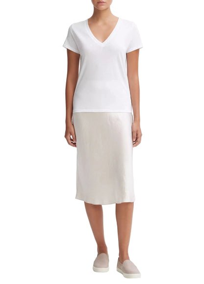 A person wearing the Vince Essential V-Neck—a white Peruvian Pima cotton T-shirt with a relaxed shape for effortless style and comfort—paired with a light-colored midi skirt and slip-on shoes, stands against a plain white background.
