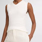 A person wearing the Vince High V-Neck Shell Tank in white and high-waisted white pants, with one hand in their pocket, stands against a plain background.