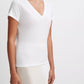 A person wearing the vince Essential V-Neck—a short-sleeved white T-shirt made from luxurious Peruvian Pima cotton—and a white skirt stands against a plain white background.