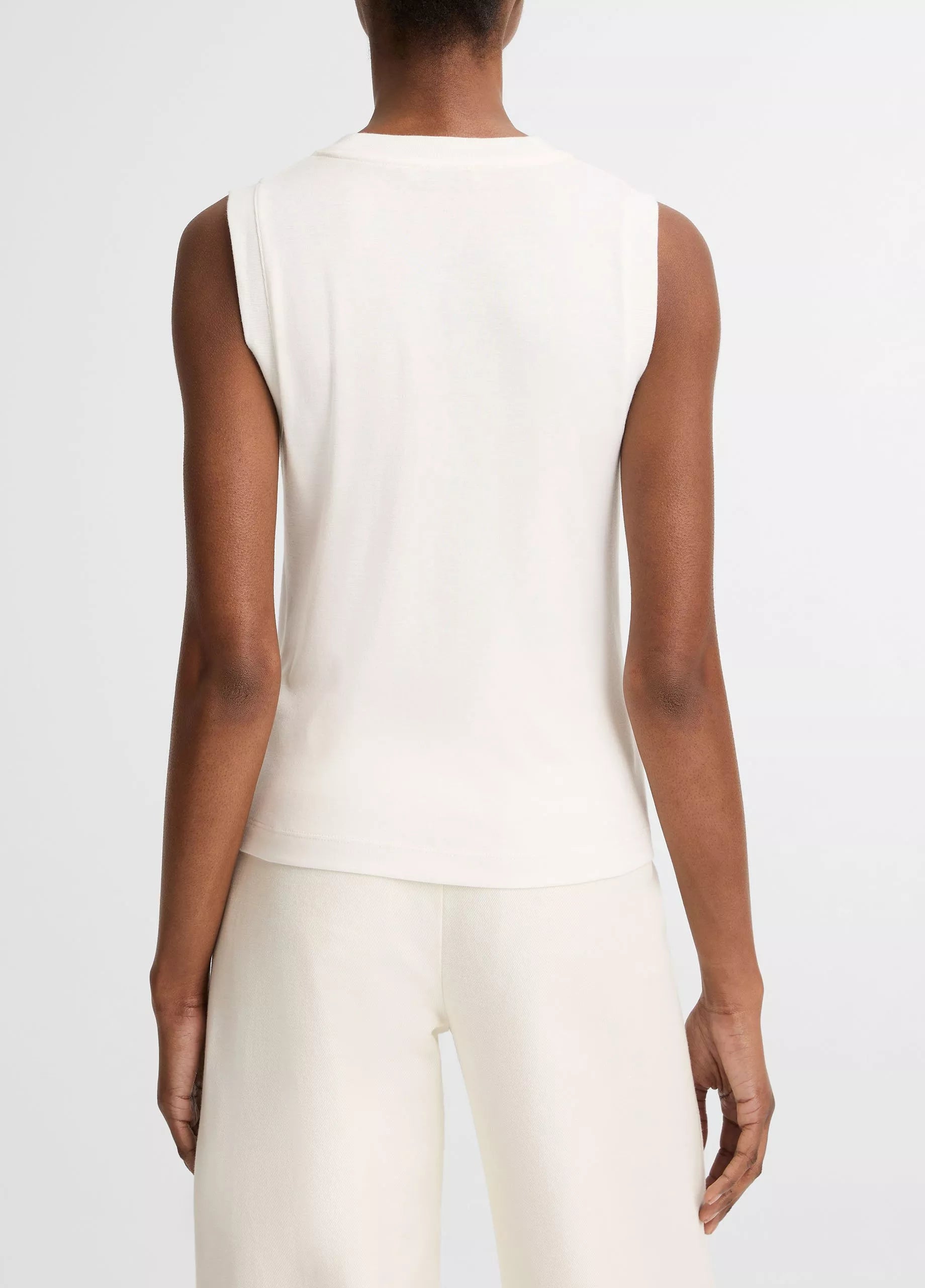 Model wears the vince High V-Neck Shell Tank, a sleeveless white top, paired with matching white pants. Shown from the back against a plain background.