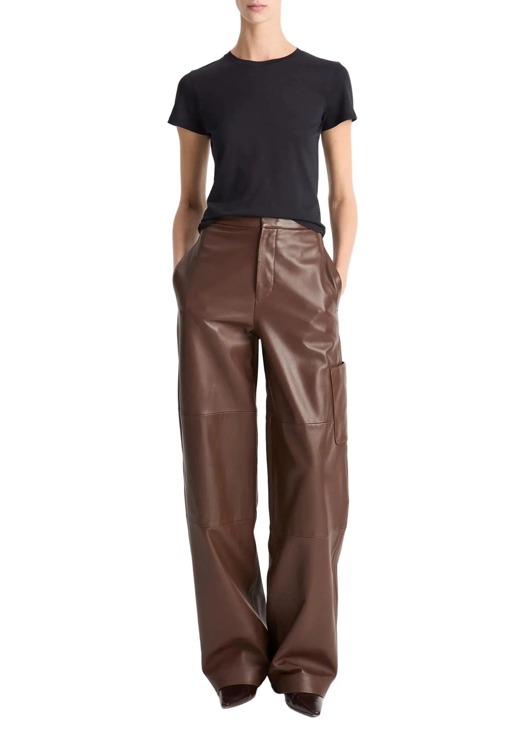 A person wearing the vince Essential Crew black short-sleeve t-shirt, crafted from soft Peruvian Pima cotton, tucked into high-waisted, wide-leg brown leather pants with hands in pockets, stands against a plain white background.