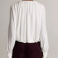 A person is shown from behind wearing the Vince Matte Jersey V-Neck Bubble Top—a long-sleeve, white blouse with gathered details—paired with dark high-waisted pants, standing against a plain background for a minimal yet subtly sophisticated look.