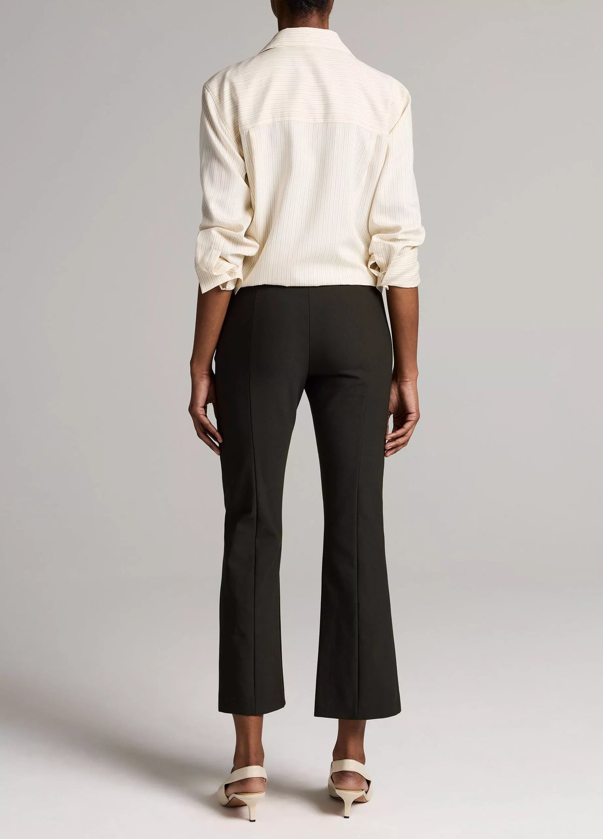 Back view of a person wearing black Niki Mid Rise Crop Flare pants and white heeled mules.