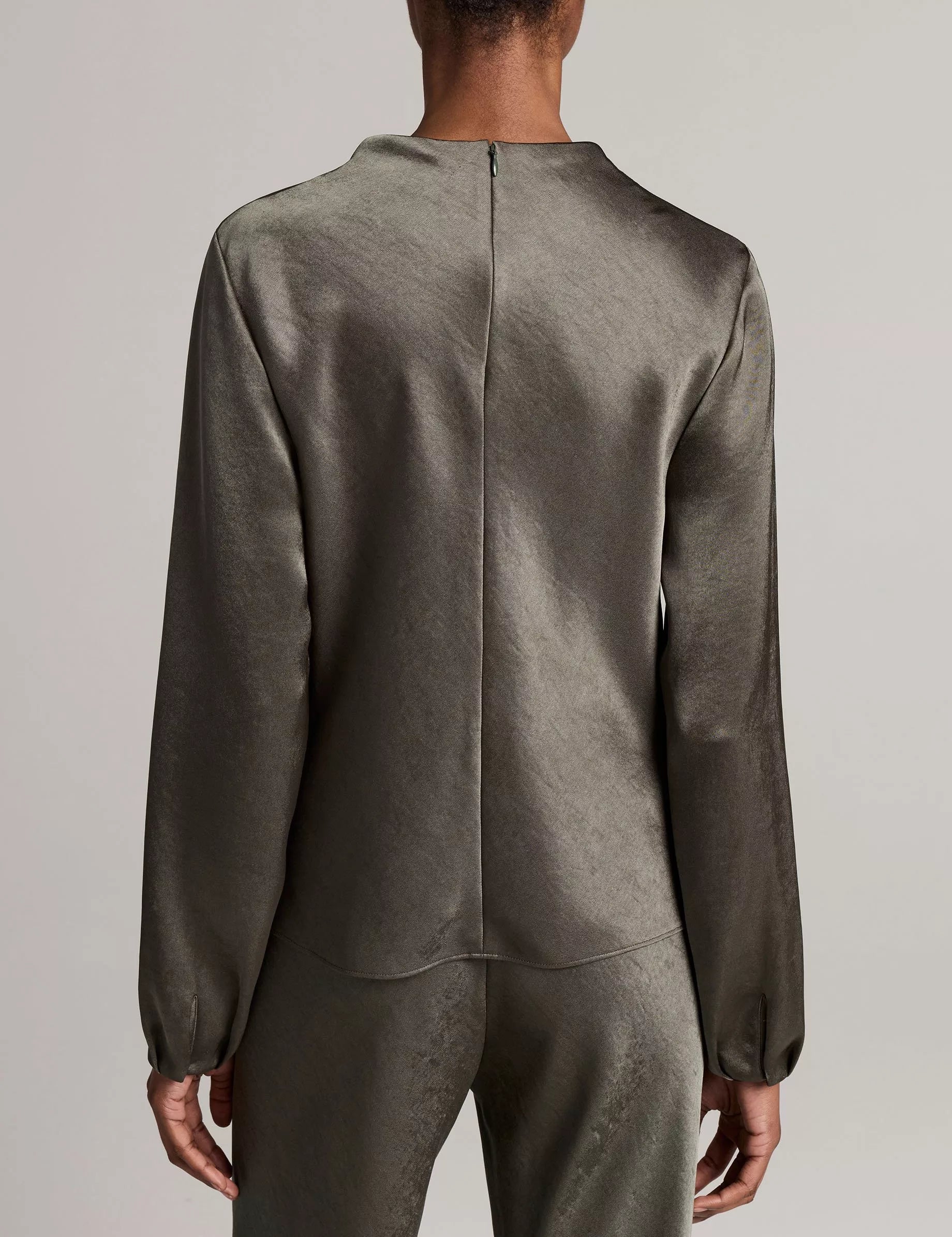 A person stands with their back to the camera, wearing the Vince Long Sleeve Draped Cowl Blouse paired with matching pants, set against a plain background.
