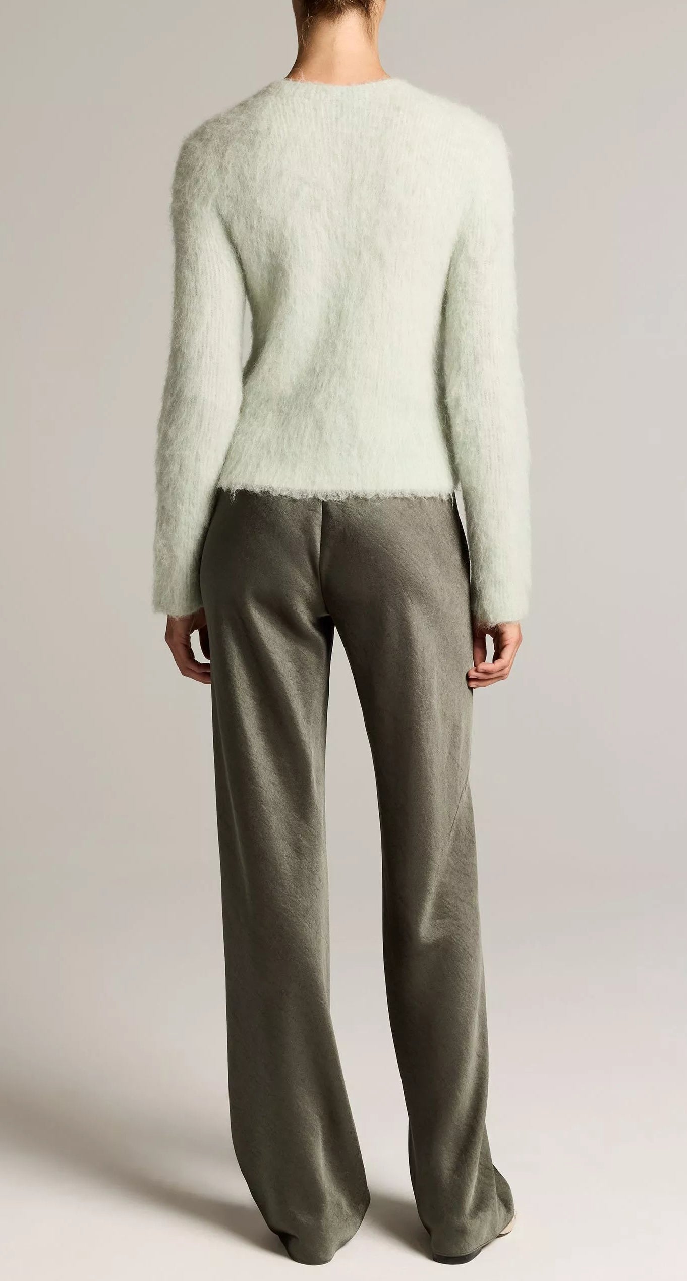A person stands facing away against a plain background, wearing a fuzzy light-colored sweater paired with the Vince Colette High Waisted Fluid Satin Bias Pant in a silky gray shade.