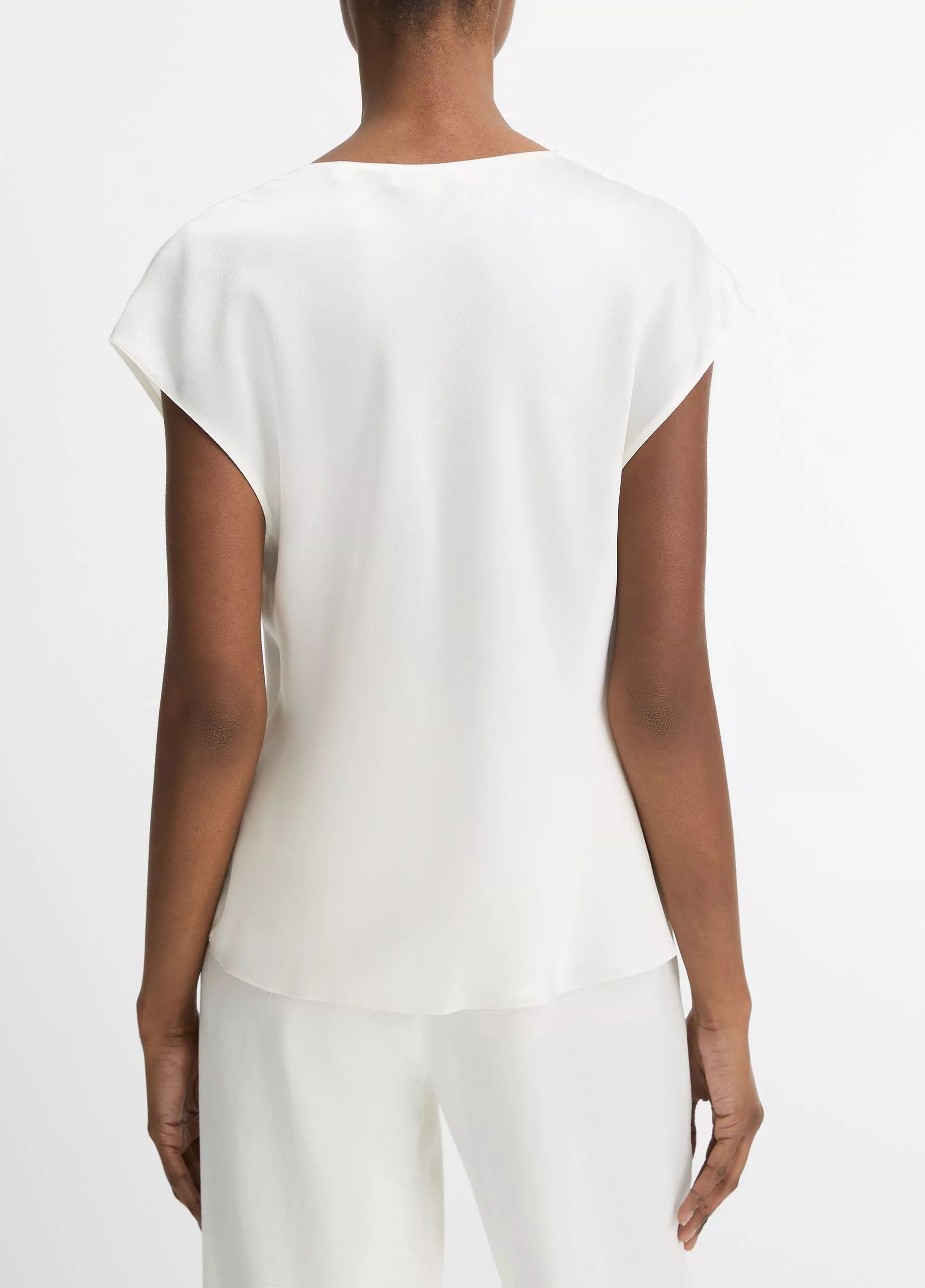 A person stands facing away, wearing the Vince Cowl Neck Cap Sleeve Silk Blouse in white, paired with matching white pants against a plain white background.