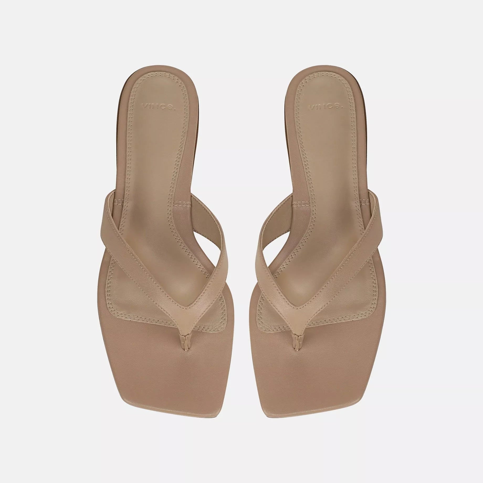 A pair of Vince San Juan Leather Thong Sandals in beige, featuring square toes, heeled design, leather straps, and a padded footbed, displayed from above on a plain white background.