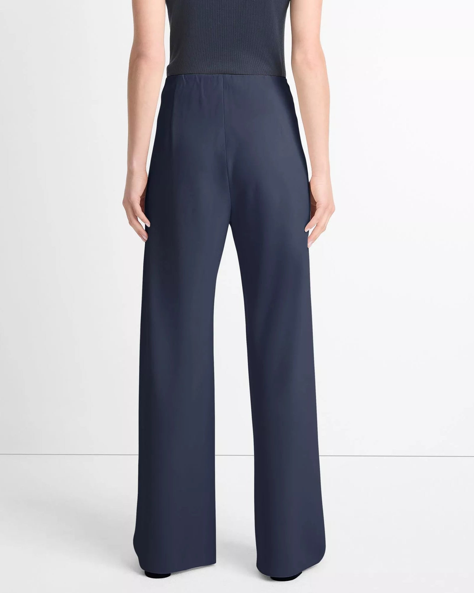A person shown from the back against a plain background wears the vince Colette High Waist Pant—navy, wide-leg crepe pants with an elastic waistband—paired with a sleeveless black top, capturing the effortless style of the design.