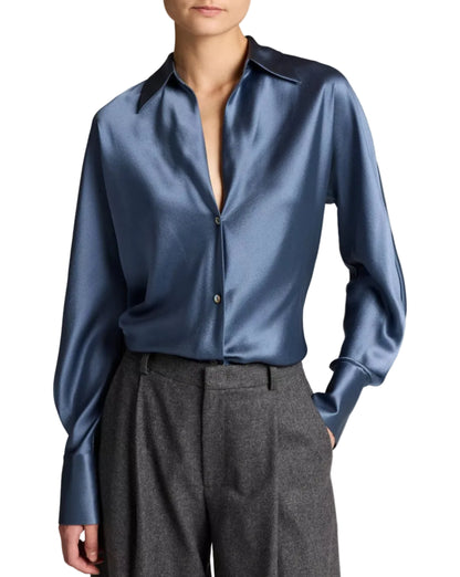 A person wearing the Vince Bias Long Sleeve Blouse, a shiny blue silk button-up with a pointed collar, tucked into high-waisted gray trousers.