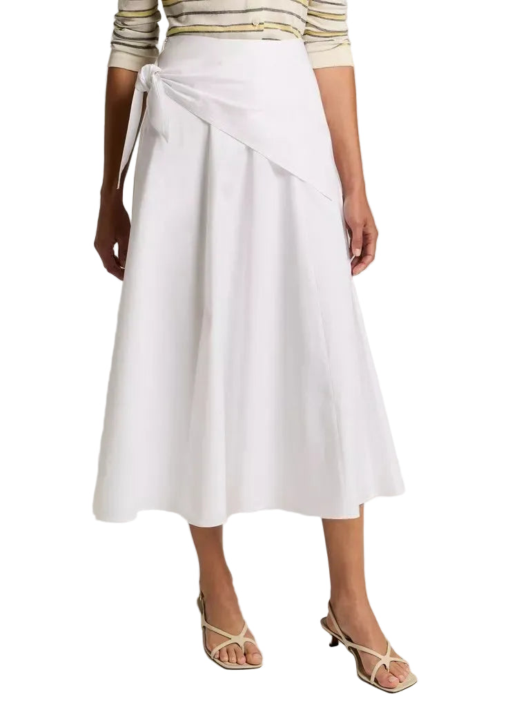 Wearing the vince Scarf Tie Skirt—a white, ankle-length cotton twill wrap skirt with a side tie—paired with a beige striped top and open-toe sandals.