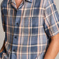 A person wearing the vince Prine Plaid Short Sleeve Cabana shirt in blue and beige plaid, with a chest pocket, partially visible from waist to neck.