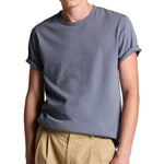 A person wearing the vince Garment Dye S/S Crew, an ultra-soft gray short-sleeve cotton jersey tee with rolled-up sleeves, paired with tan pants, stands against a white background. Their face is partially out of frame.