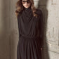A person wearing sunglasses and a long sleeve draped cowl blouse by vince stands against a textured concrete wall.