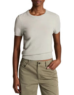 A person wears the Vince Relaxed Short Sleeve Crew Sweater in light gray—crafted from lightweight wool-cashmere in a fine-gauge knit—with khaki pants and one hand in a pocket, set against a white background.