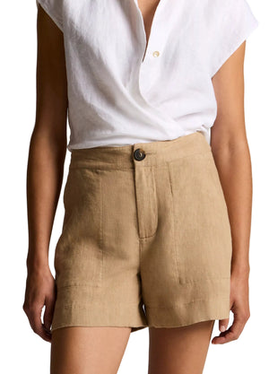 A person wearing a white short-sleeve button-down shirt tucked into the vince Mid Rise Hemp Short, a pair of high-waisted, tan breathable shorts with a relaxed silhouette, complete with front button and pocket detailing.