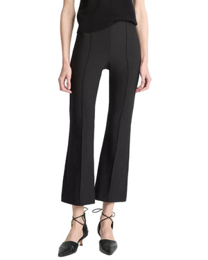 A person is shown from the shoulders down against a white background, wearing black Niki Mid Rise Crop Flare Pants by vince, crafted from luxurious Italian cotton-blend bi-stretch fabric, paired with black pointed-toe lace-up shoes.