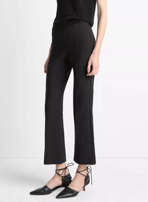 A person wearing Vince’s Niki Mid Rise Crop Flare Pant in black Italian cotton-blend, featuring pintuck legs, paired with black pointed-toe ankle-strap shoes and standing against a plain white background.