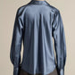 A person is seen from the back wearing the Vince Bias Long Sleeve Blouse in blue, paired with gray pants, standing against a plain light background.