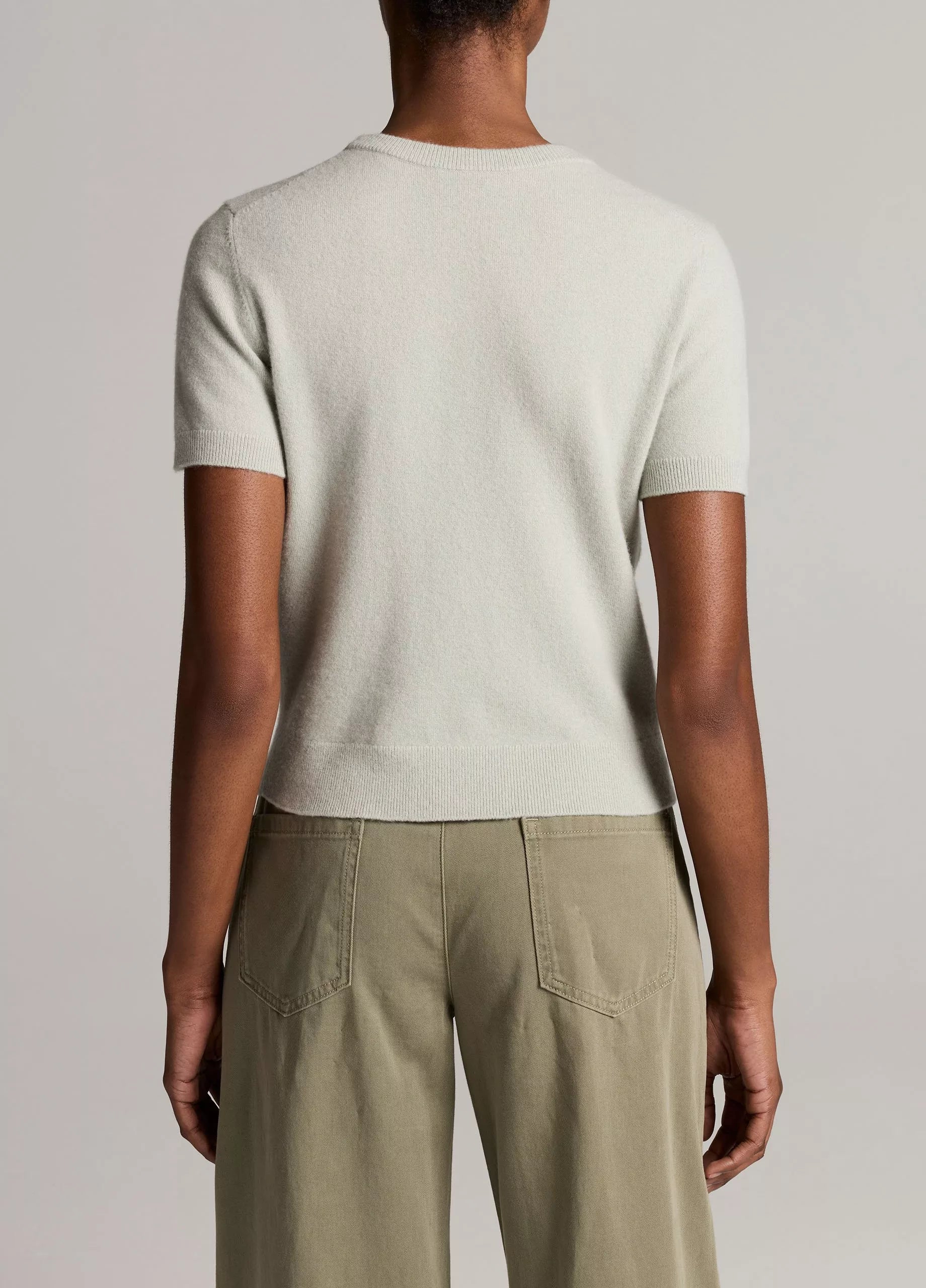 A person stands facing away, wearing the Vince Relaxed Short Sleeve Crew Sweater—crafted from lightweight wool cashmere—and olive green pants. The background is plain and neutral.