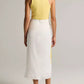 A person stands barefoot, facing away in a plain studio, wearing a yellow sleeveless top paired with the Painted Abstract Draped Skirt by vince—a white midi twill skirt crafted from LENZING™ ECOVERO™ viscose that lends an elegant touch to the simple ensemble.