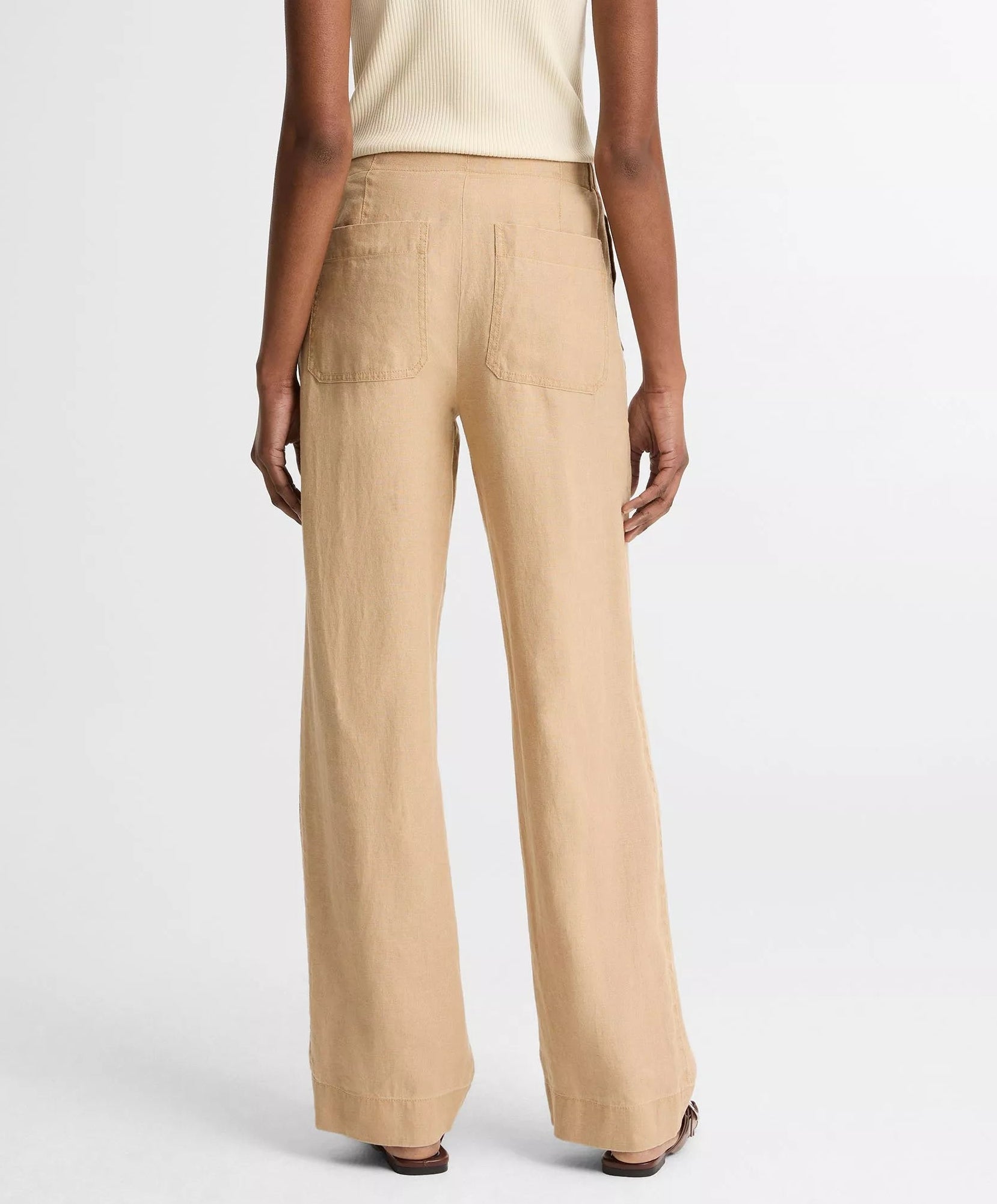 A person wearing vince’s Hemp Utility Pant in beige, featuring a relaxed silhouette, paired with a sleeveless ribbed top, is shown from the back against a plain white background.