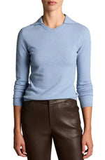 A person wearing the Vince Long Sleeve High V-Neck Polo Sweater in light blue, paired with dark brown pants, stands against a plain background.