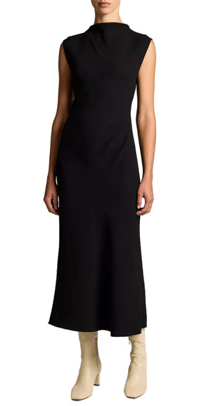 A person wearing the vince Draped Funnel Neck Dress—a sleeveless, ankle-length black matte crepe midi dress with a ruched waist—paired with light-colored ankle boots, standing against a white background.