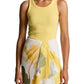 A woman wearing the Vince Ribbed Scoop Neck Tank, a sleeveless yellow finely ribbed top crafted from a soft cotton-modal blend, paired with a white skirt featuring a yellow and green floral print, stands against a plain background.